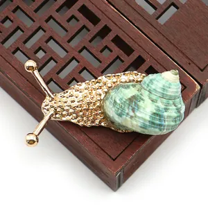 Detalle macro del broche de caracol dorado con una concha de mar natural verde en espiral