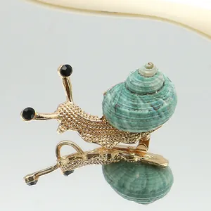 Detalle de un broche de caracol dorado con concha verde y ojos de piedras preciosas negras