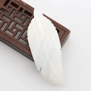 Macro detail of hand-carved white mother of pearl shell pendant in realistic feather shape