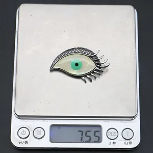 Detailed view of evil eye shell pendant on digital scale showing a weight of 7.55 grams