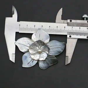Detail view of a shell carved flower brooch with a center pearl measured by a caliper