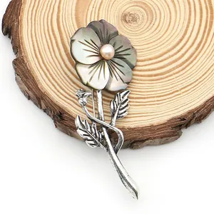 Detail of flower brooch with dark shell petals and a pink pearl on a wooden texture