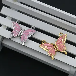 Pendentifs papillons émaillés roses avec bords or et argent sur une mini chaise blanche