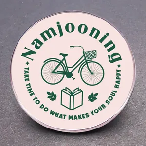 Detail der Namjooning-Anstecknadel mit Fahrrad- und Buchmotiven auf hellem Rosa