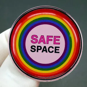 Rainbow Safe Space enamel pin badge featuring a circular metal design held by a hand