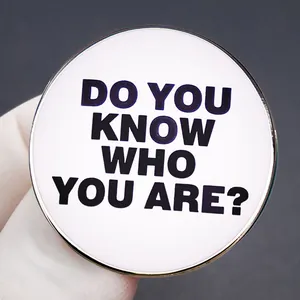 Runder Metall-Anstecker mit 'DO YOU KNOW WHO YOU ARE?' Text, gehalten von einem Handschuh