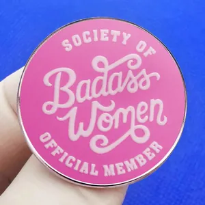 Pink enamel Badass Women Society pin badge shown against a blue textured background