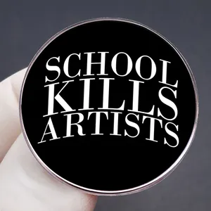Spilla tonda nera con slogan bianco School Kills Artists tenuta da una mano guantata