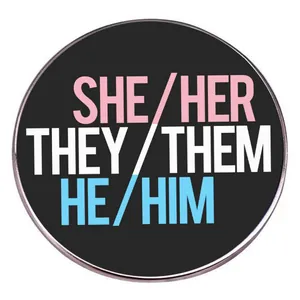 Pin redondo con pronombres She/Her, They/Them, He/Him sobre fondo negro y borde de metal