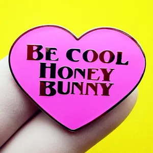 Pin esmaltado de corazón rosa con texto Be Cool Honey Bunny sobre un fondo amarillo