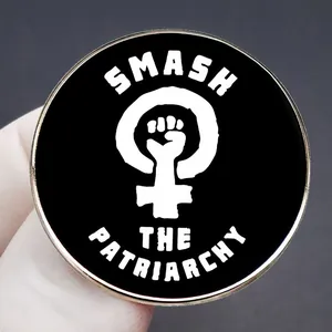Spilla Smash the Patriarchy con simbolo femminista e pugno tenuta a mano su fondo grigio