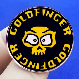Round Goldfinger enamel pin featuring a yellow skull on a black punk rock music badge