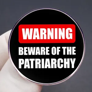Warning Beware Of The Patriarchy feminist circular metal pin badge held by a gloved hand