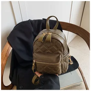 Detail view of quilted olive green mini backpack with golden metal zippers on a wooden chair