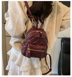 Detail of burgundy quilted mini backpack with gold zippers shown on a shoulder