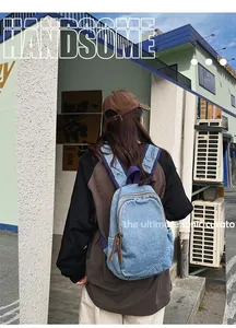 Detail of light blue washed denim backpack shown on model in an outdoor street setting