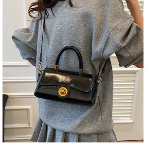 Détail d'un sac à main en cuir verni noir brillant avec fermoir doré sur un modèle