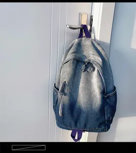 Détail d'un sac à dos en denim délavé avec sangles mauves sur une poignée de porte