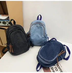 Three denim backpacks in black, light blue, and dark blue on a white table with books