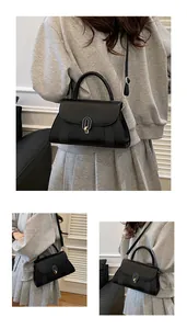 Detail of black crossbody bag with gold oval lock and textured woven side panels