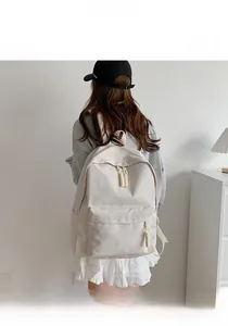 Detail of minimalist cream backpack showing woven rope zipper pulls on the front pocket