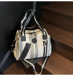 Detail of grey striped canvas travel bag with letter N logo and textured zip pocket