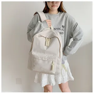 Minimalist beige backpack with woven rope zipper pulls shown on a model in a casual outfit