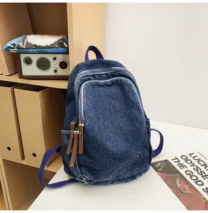 Detail of blue washed denim backpack with brown faux leather pull tabs and front pocket