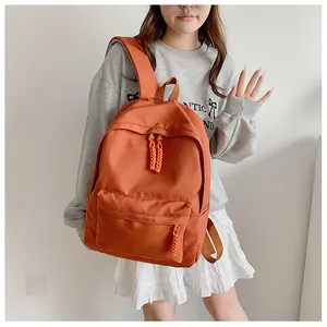 Detail view of the orange nylon backpack showing the front zipper pocket and woven puller