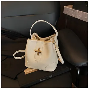 Detail of cream white bucket bag featuring litchi texture and gold metal turn-lock closure