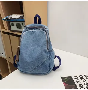 Detailed close-up of light blue denim backpack with dark blue straps and leather zipper pulls