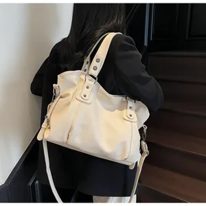 Detail of a beige leather tote bag with silver studs and adjustable strap on a shoulder
