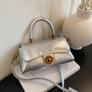 Petit sac carré argenté texturé avec fermoir tournant doré sur décor blanc épuré