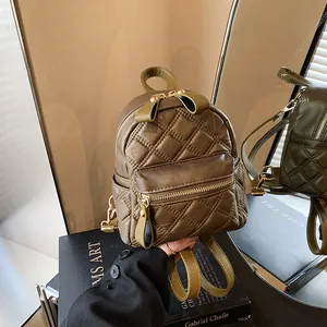 Olive green quilted mini backpack with gold zippers shown in a stylish hand-held pose