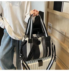 Detail of striped woven travel tote featuring logo patch and reinforced leather handles