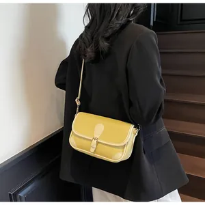 Détail d'un sac bandoulière en cuir litchi jaune avec bordure blanche porté par un mannequin