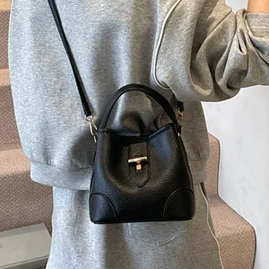 Minimalist black lychee texture leather bucket bag with gold swivel lock and strap