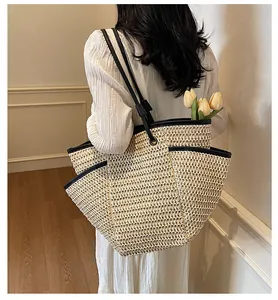 Detail of a large woven straw tote bag with black contrast piping and slim shoulder straps