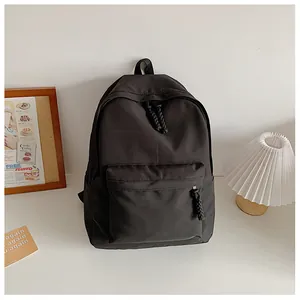 Minimalist black nylon backpack featuring large front zipper pocket and woven pull tabs