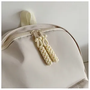 Close-up of dual zippers with woven pull cords on a minimalist cream-white backpack