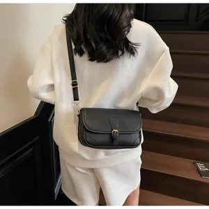 Détail du sac bandoulière en cuir grainé noir avec sangle réglable sur tenue blanche