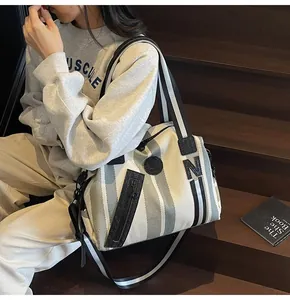 Close-up of striped canvas tote bag featuring front zipper pocket and leather accents