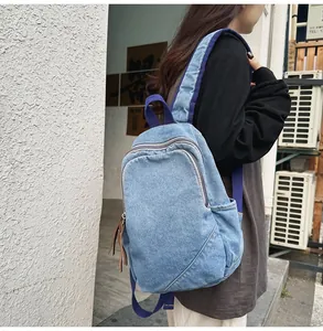 Detail of light blue washed denim backpack featuring purple fabric straps and leather zippers
