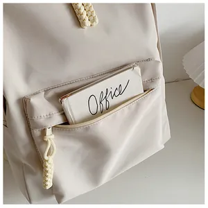 Detail of beige nylon backpack featuring a woven zipper pull and spacious front pocket