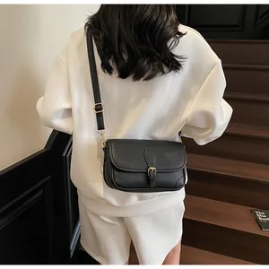 Détail du sac bandoulière noir en cuir grainé avec boucle dorée sur tenue blanche