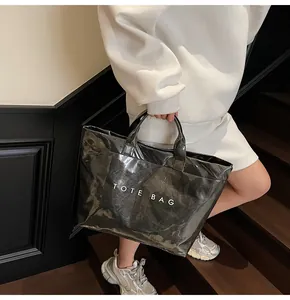 Model carrying a glossy black tote bag with white text print on a wooden staircase