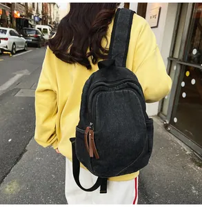 Detailed view of black denim backpack with textured fabric and leather zipper pulls on a model