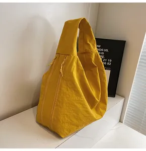 Detail of a bright yellow crescent tote bag showing wrinkled nylon texture and side zippers