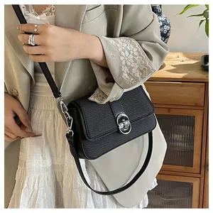 Close-up of black textured crossbody bag with silver oval twist lock on a beige blazer