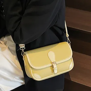 Sac bandoulière en cuir jaune pâle avec rabat et boucle sur escalier en bois